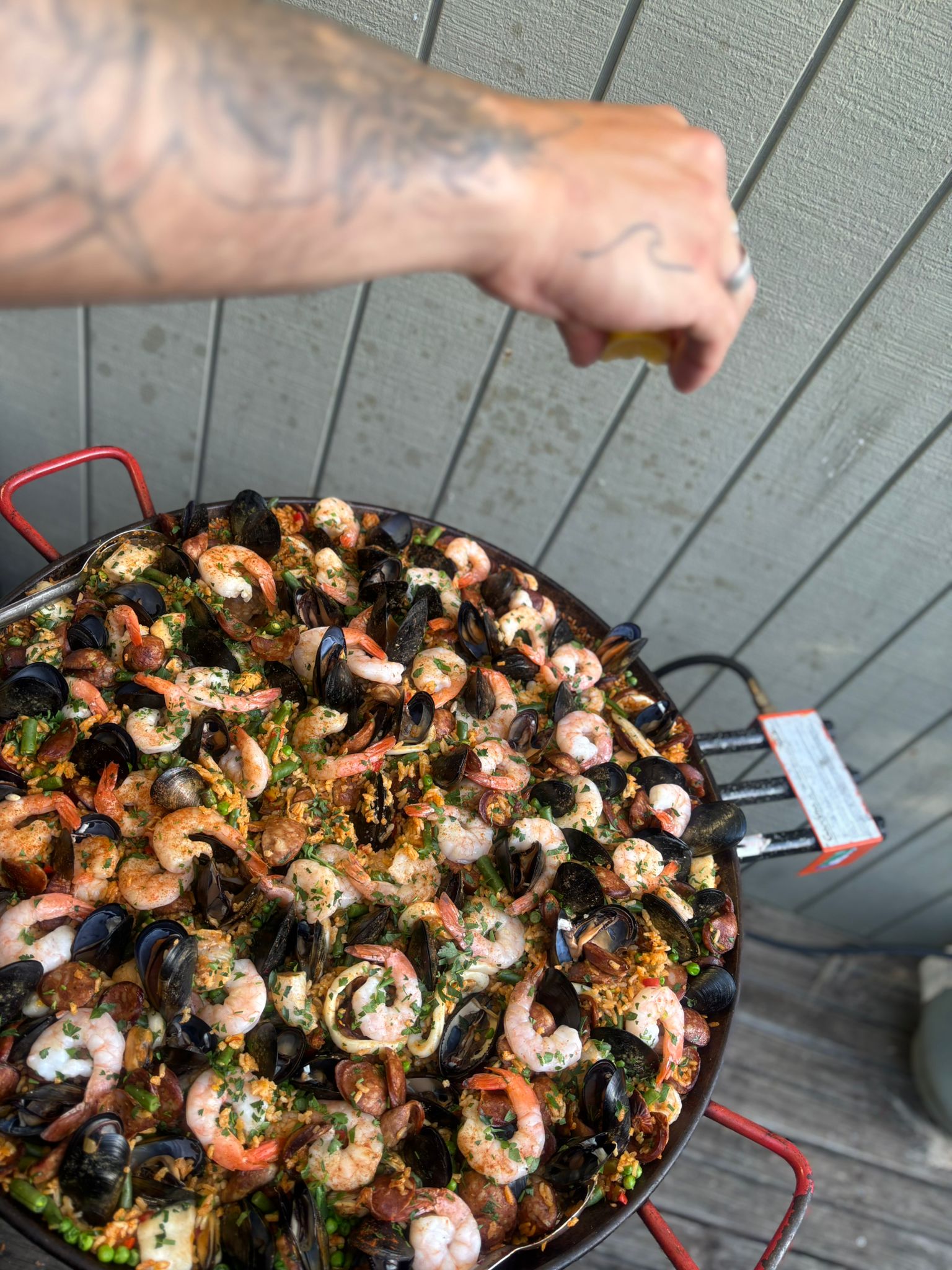A hand squeezing lemon juice over a fresh seafood paella